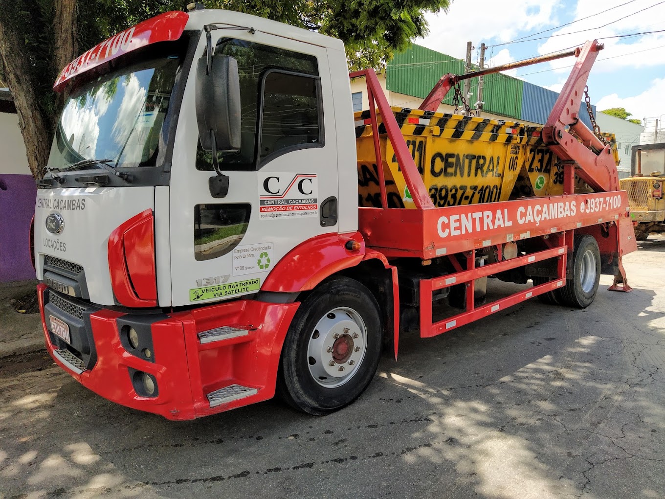Caminhão vermelho da Central Caçambas transportando caçamba estacionária
